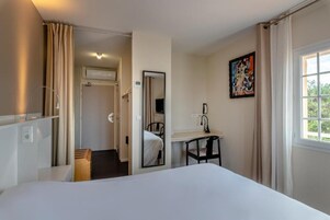 Una habitación de hotel con cama, escritorio, silla, espejo y ventana.