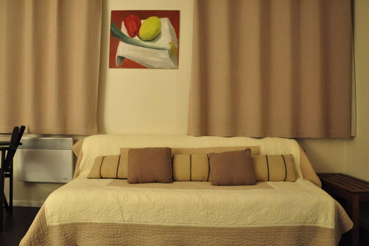 A hotel room with a large bed, beige curtains, and a painting of vegetables on the wall.