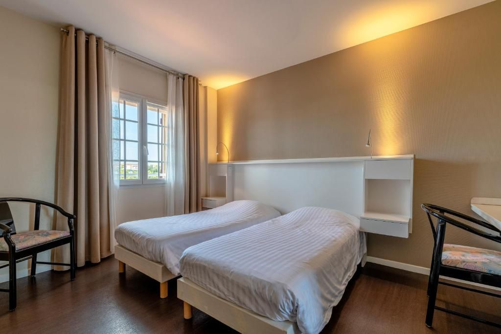 Una habitación con dos camas, una silla, un escritorio y una ventana con cortinas.