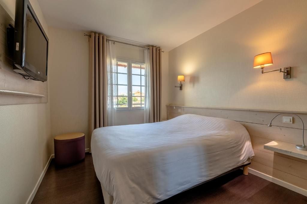 Habitación de hotel con cama, televisión montada en la pared, ventana con cortinas e iluminación en la pared.