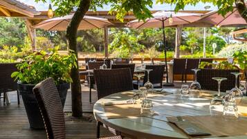 An outdoor dining area with round tables, wicker chairs, and umbrellas providing shade.