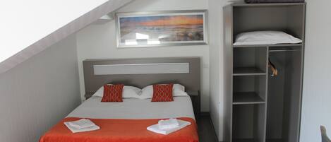 A neatly made bed with a red blanket and pillows, a gray wardrobe, and a framed picture on the wall.
