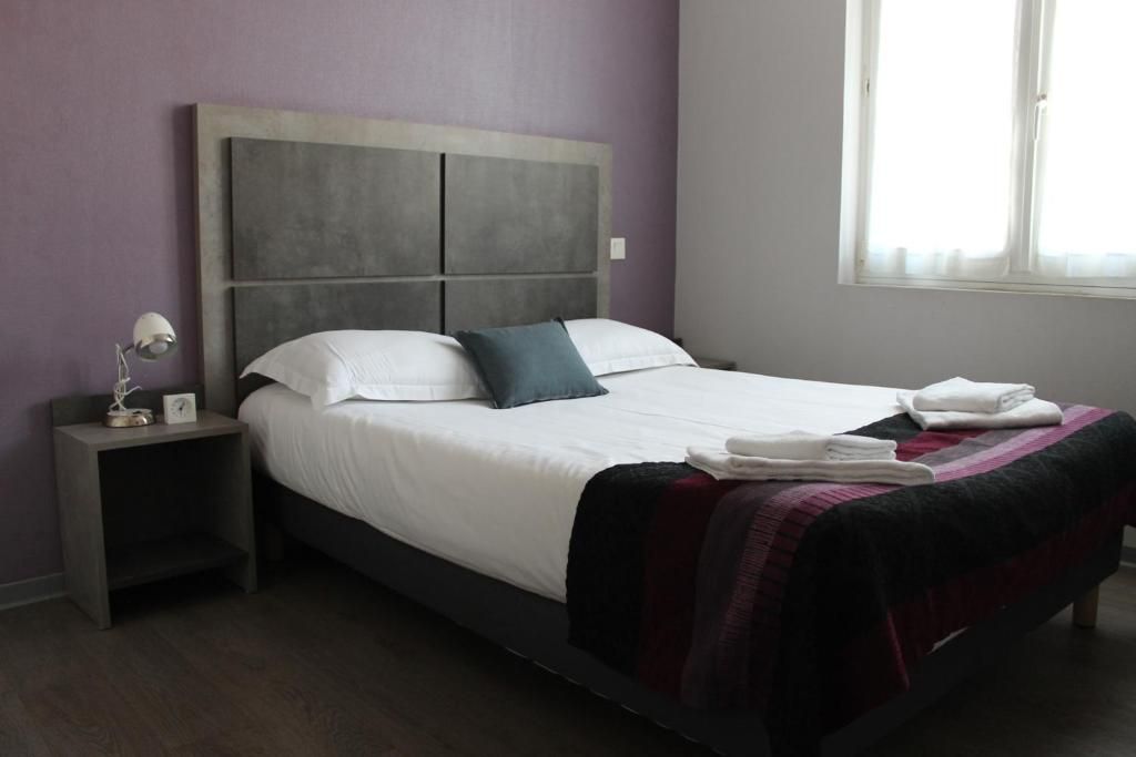 Una cama bien tendida con un cabecero, una mesita de noche con una lámpara y una ventana con cortinas.