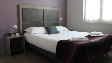 Una cama bien tendida con un cabecero, una mesita de noche con una lámpara y una ventana con cortinas.