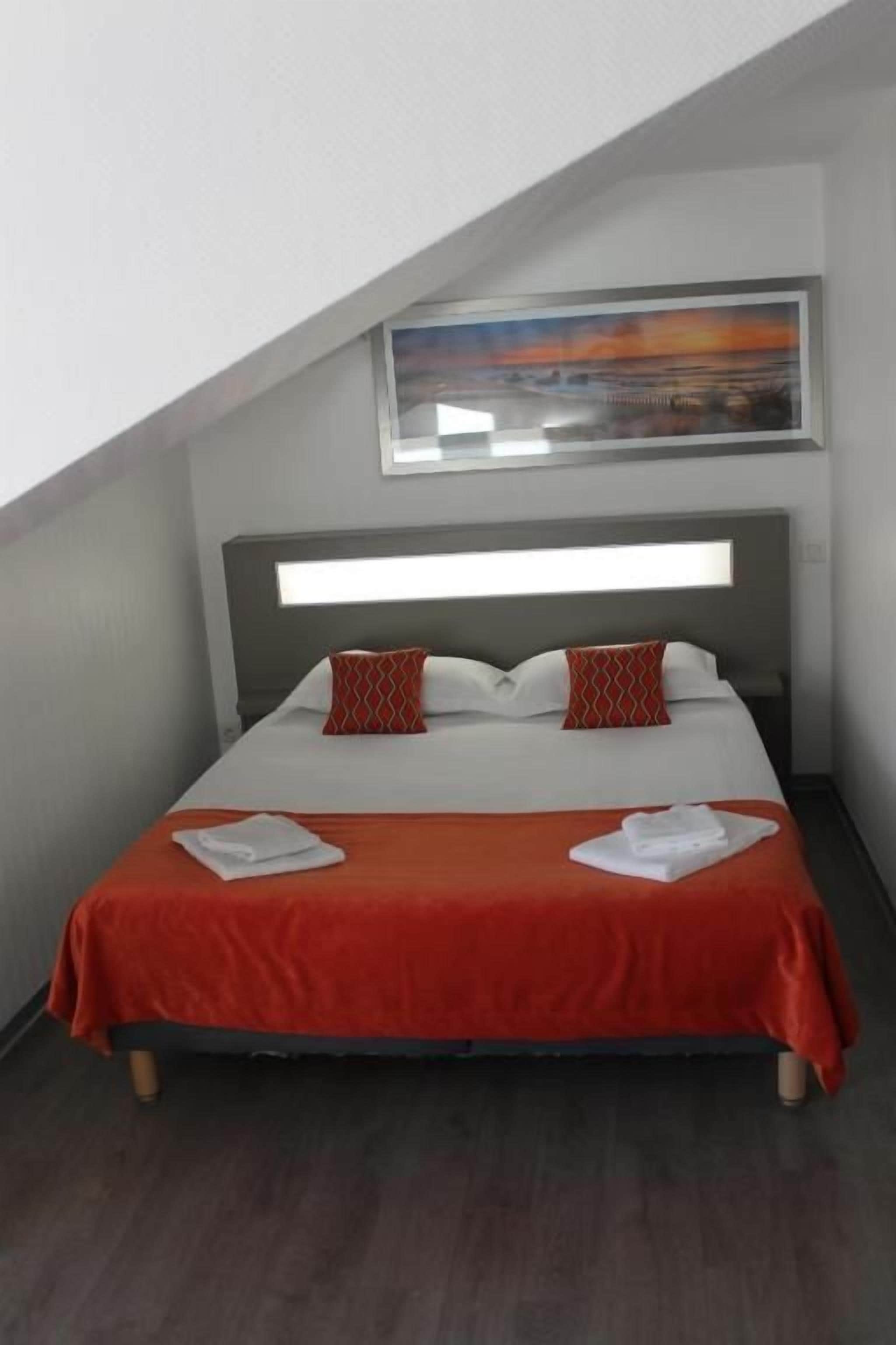 A hotel room with a bed, a headboard, a painting above the bed, and a window.