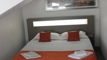 A hotel room with a bed, a headboard, a painting above the bed, and a window.
