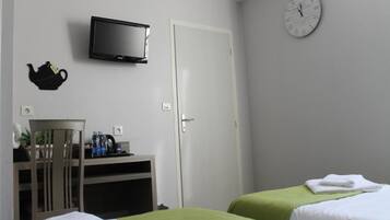 Habitación de hotel con dos camas, televisión, reloj, hervidor de agua y un escritorio pequeño con una silla.