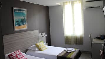 Habitación de hotel con dos camas, un cartel en la pared, una ventana con cortinas y un equipo de aire acondicionado.