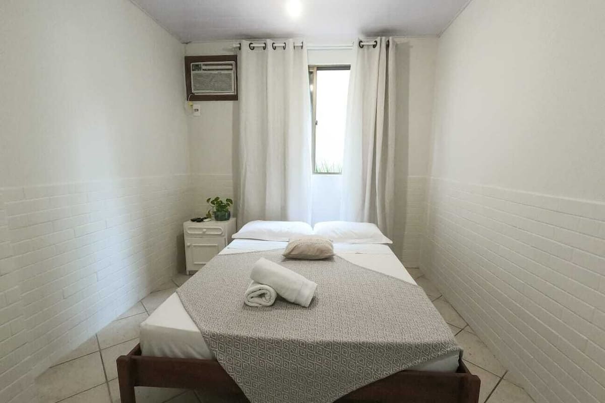 A small, neatly arranged bedroom with a single bed, a nightstand, and a window with curtains.