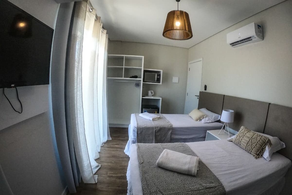 A hotel room with two beds, a television, a wardrobe, a microwave, and an air conditioning unit.