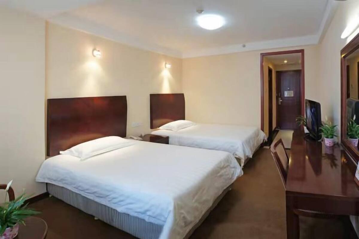 Ein Hotelzimmer mit zwei Betten, einem Holztisch, einem Fernseher und Wandleuchten.