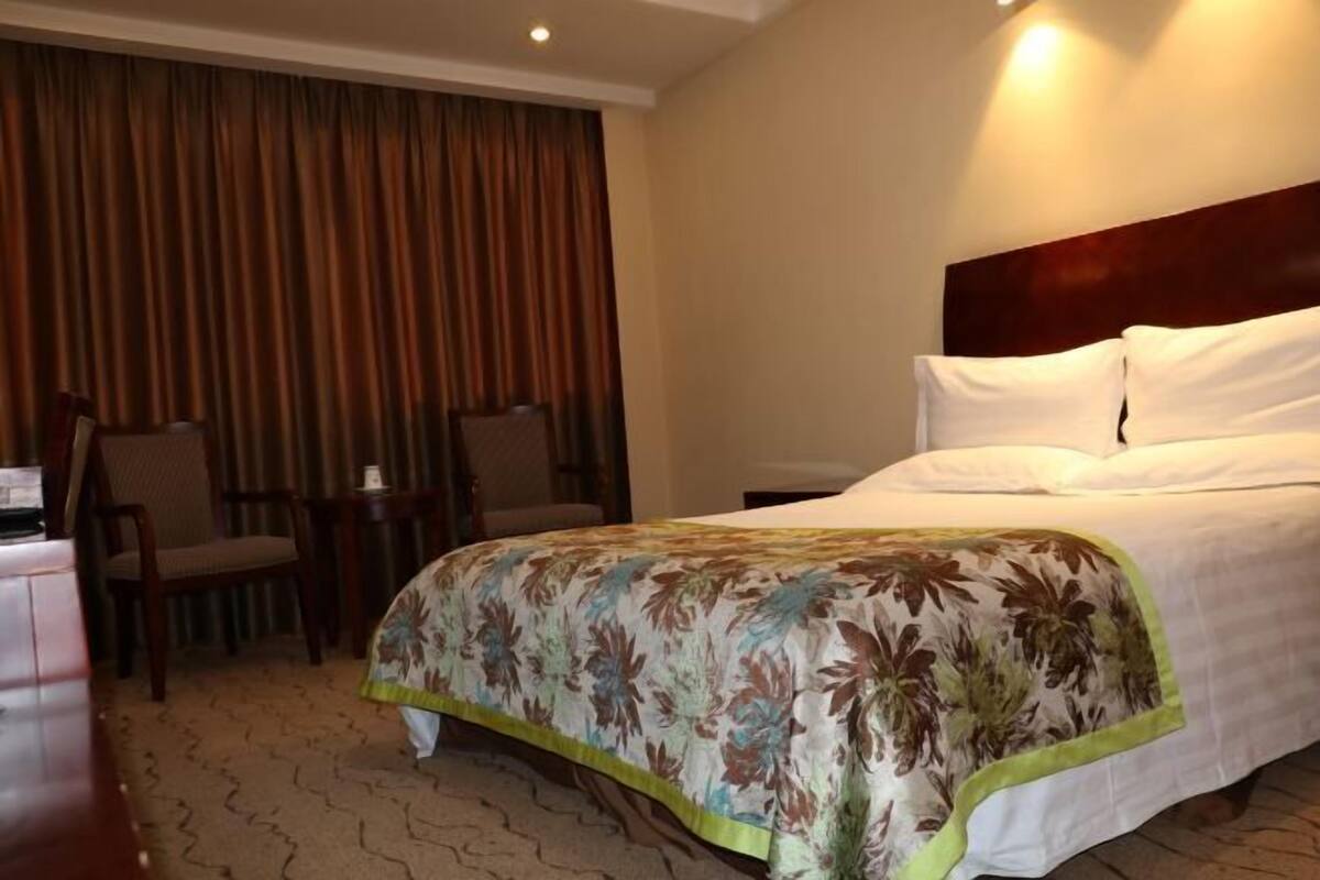 Ein Hotelzimmer mit Bett, Stuhl, kleinem Tisch und Vorhang.