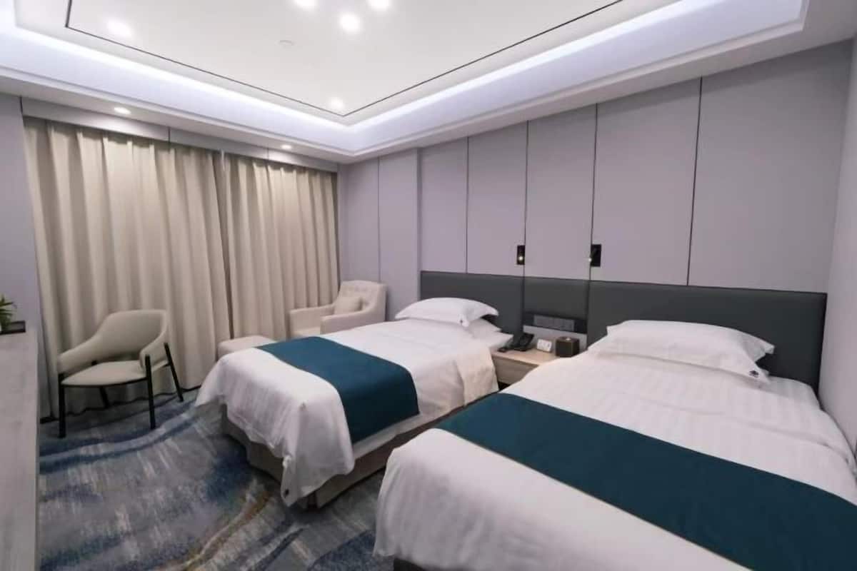 A hotel room with two beds, a chair, a desk, and a large window with curtains.