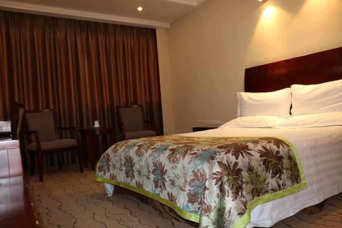 A hotel room with a bed, a chair, a small table, and a curtain.