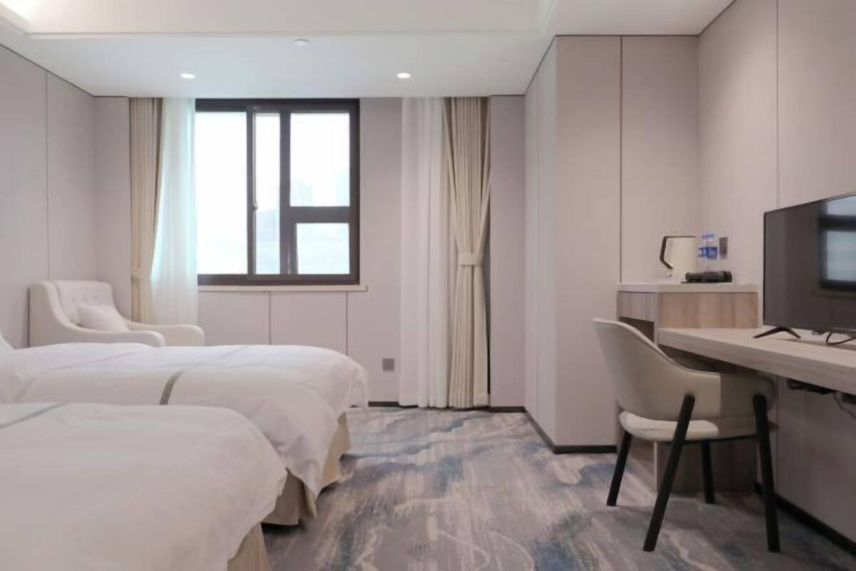 Ein Hotelzimmer mit zwei Betten, einem Schreibtisch, einem Stuhl, einem Fernseher und einem Fenster mit Vorhängen.