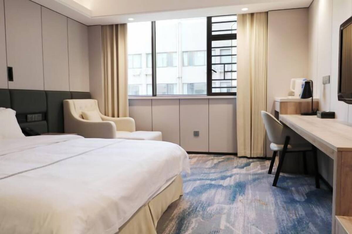 Ein Hotelzimmer mit einem großen Bett, einem Schreibtisch, einem Stuhl und einem Fenster mit Vorhängen.