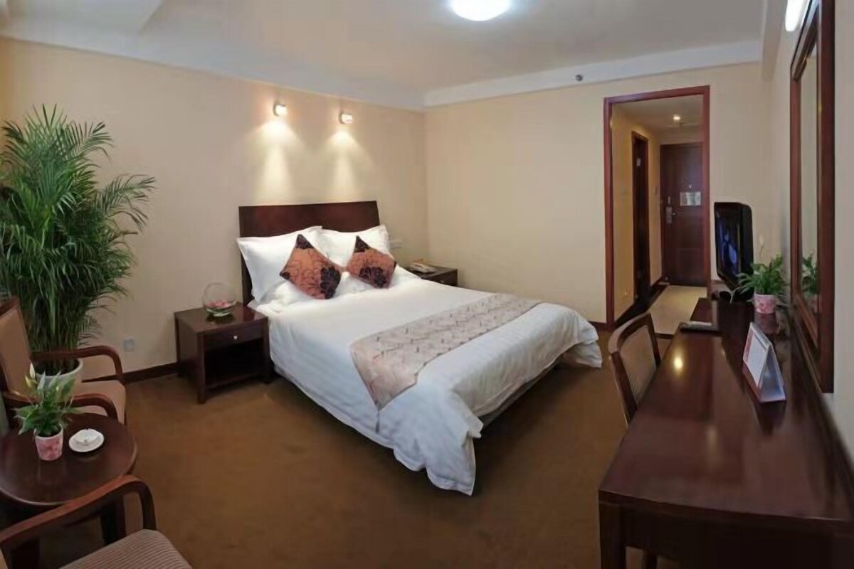 A hotel room with a bed, bedside tables, a desk, chairs, a potted plant, and a mirror.