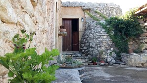 A rustic stone building with a wooden door, potted plants, and a stone wall. - Bendeni Cottage (Chania)