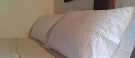 Una cama con sábanas blancas y una almohada decorativa.
