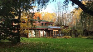 Un chalet rustique avec un toit végétalisé, entouré d’un jardin luxuriant et d’arbres aux feuilles d’automne.
