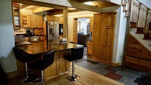 Une cuisine avec des meubles en bois, un coin bar avec des tabourets et un sol carrelé en pierre.