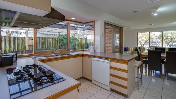 A modern kitchen with a gas stove, dishwasher, and a dining area with a table and chairs. - SHORE THING - FAMILY BEACH RETREAT  (Tootgarook)