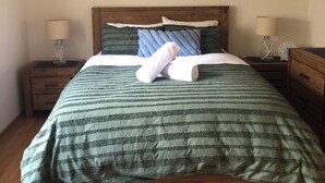 A bed with a green striped bedspread, two pillows, and a rolled towel. There is a wooden headboard and a painting above the bed. - SHORE THING - FAMILY BEACH RETREAT  (Tootgarook)