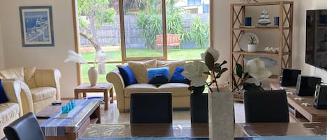 A spacious living room with a large window, a sofa, a dining table with chairs, and a TV.