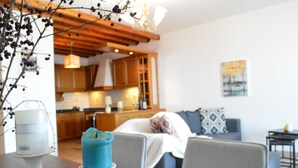 A modern kitchen with wooden cabinets, a dining area with a table and chairs, and a living room with a sofa and a painting on the wall. - Akti Posidonos (Agios Nikolaos)