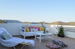 A sunlit balcony with a white sofa, a lounge chair, and a small table. - Akti Posidonos (Agios Nikolaos)