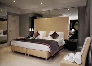 Una habitación de hotel moderna con una cama grande, mesitas de noche, un espejo y una zona de estar con toallas.