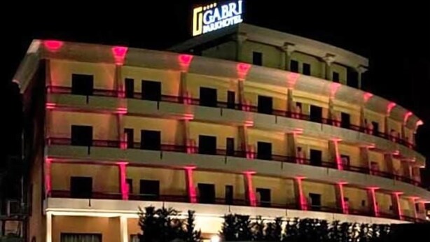 Ett hotell med flera våningar, balkonger, en skylt som visar att det är ett hotell och en väl upplyst fasad.