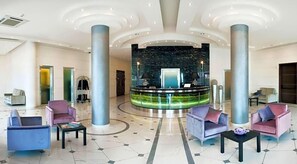A spacious lobby with a reception desk, seating area, and a circular water feature.
