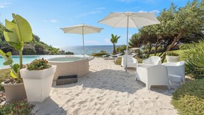 En terrasse ved stranden med udendørs møbler, jacuzzi og parasoller.
