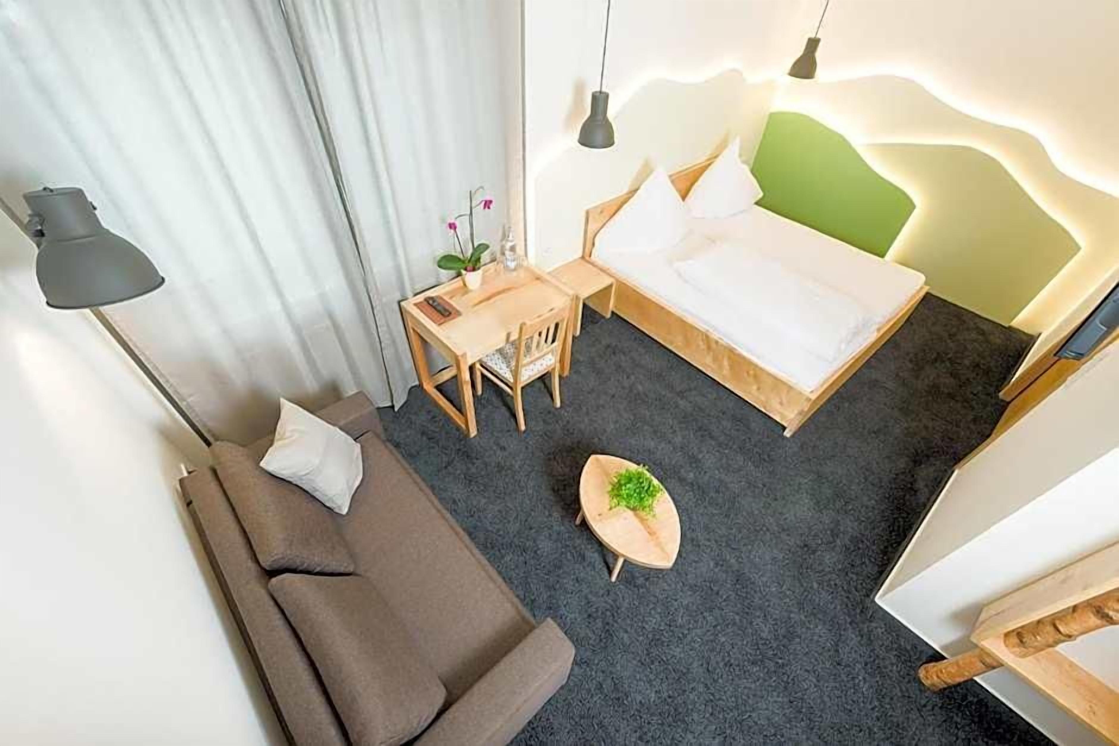 A hotel room with a bed, a sofa, a desk, and a small table with a plant.