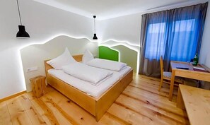 Una habitación con una cama de madera, una mesita pequeña, una silla y un escritorio con una lámpara.