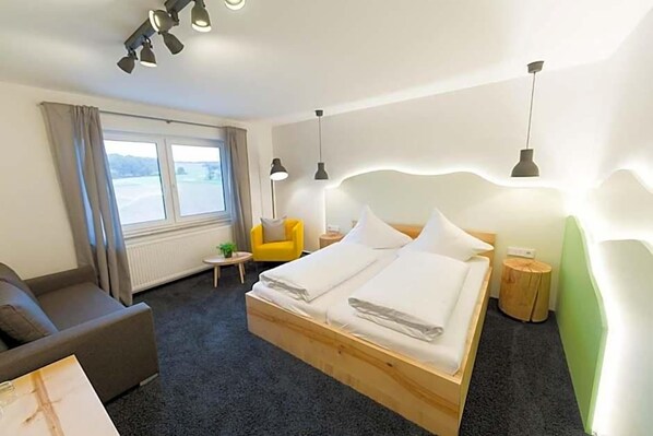 A hotel room with a bed, a sofa, a chair, and a window with curtains.