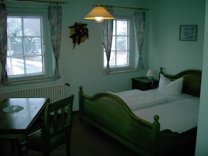 A bedroom with a single bed, a bedside table with a lamp, a chair, and a window with curtains. - Landhotel Am Fuchsbach (Berga/Elster)
