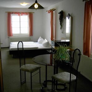 A hotel room with a bed, a desk with a chair, a round table, and a potted plant. - Landhotel Am Fuchsbach (Berga/Elster)