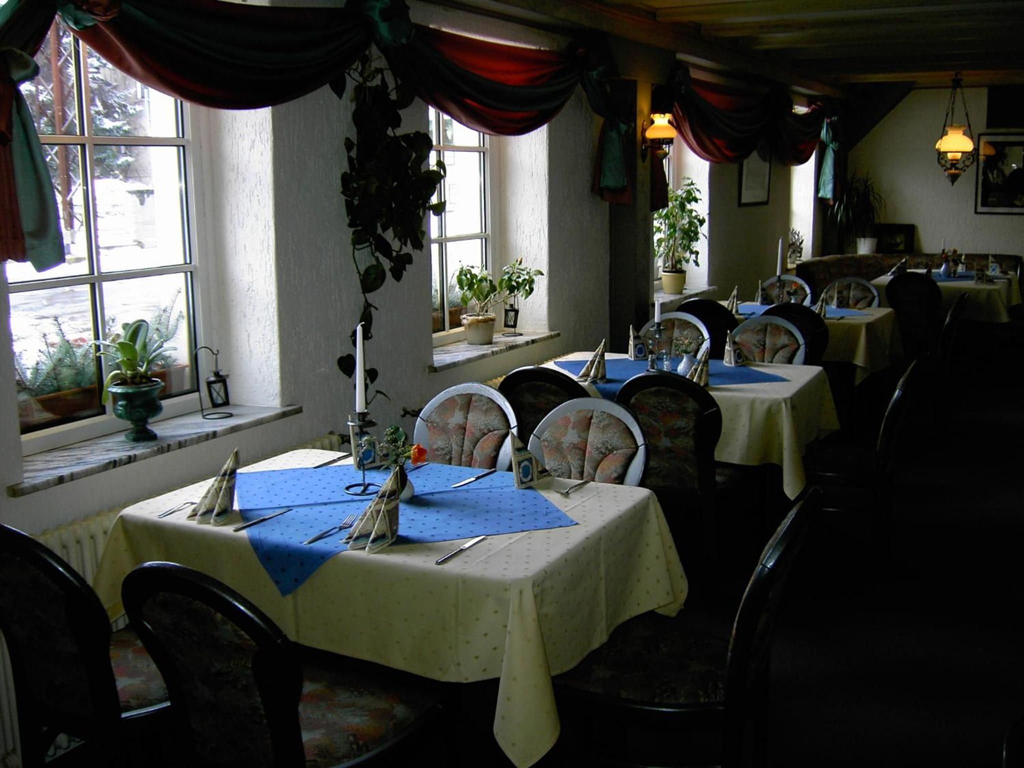A restaurant with multiple tables set for dining, each with a blue tablecloth and white tablecloths.