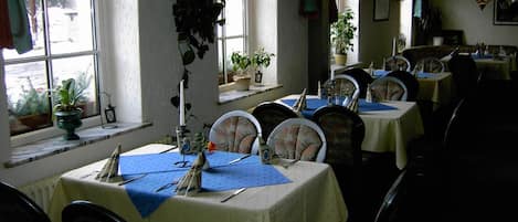 A restaurant with multiple tables set for dining, each with a blue tablecloth and white tablecloths.