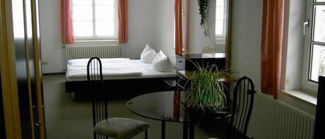 A bedroom with a bed, a desk, two chairs, a radiator, and a window with curtains.