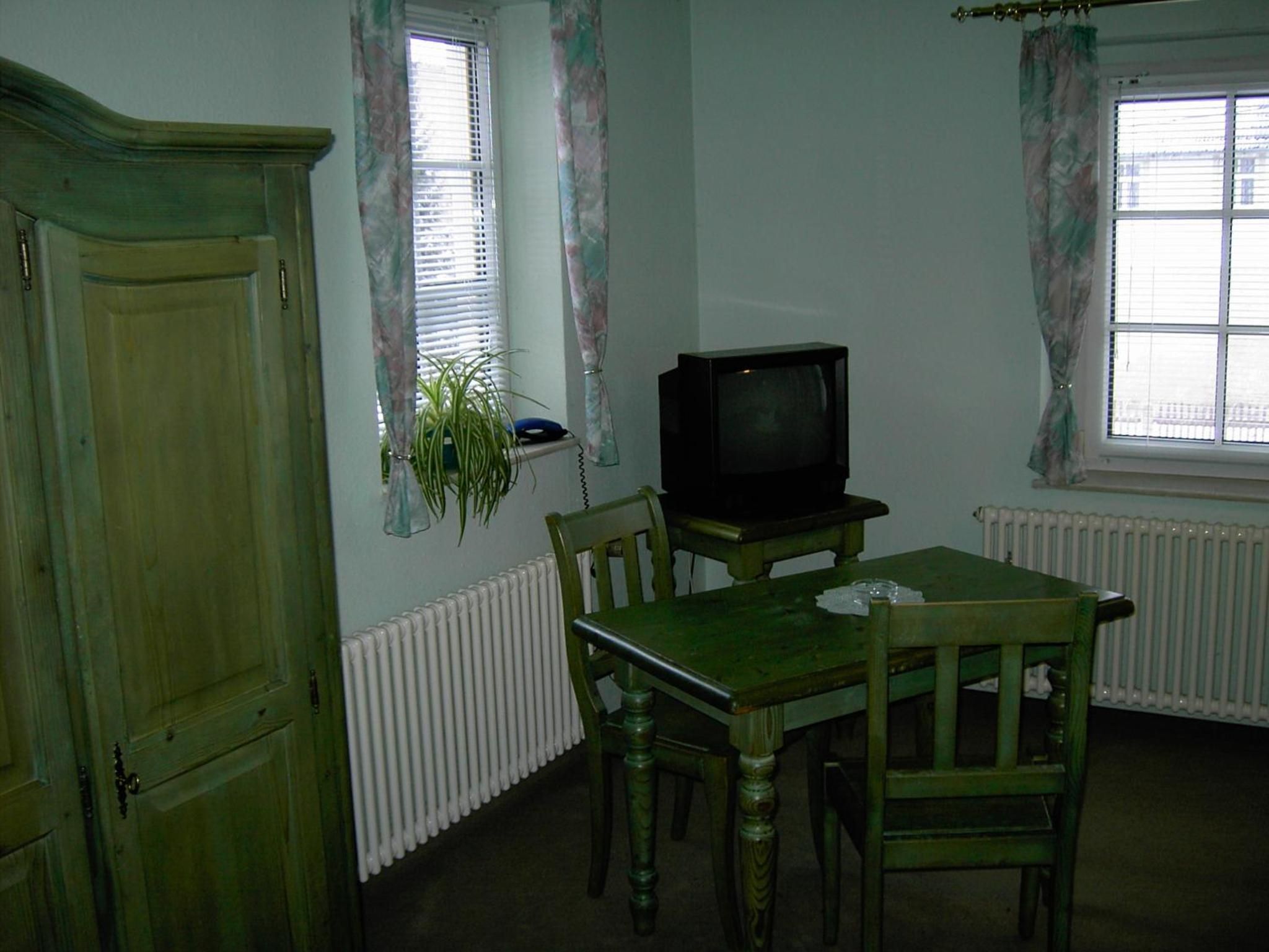 A room with a wooden table, two chairs, a television, and a radiator.