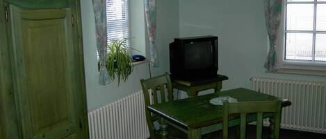 A room with a wooden table, two chairs, a television, and a radiator.