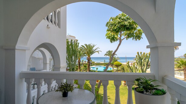 Un balcon avec vue sur la mer, une piscine et des plantes tropicales.