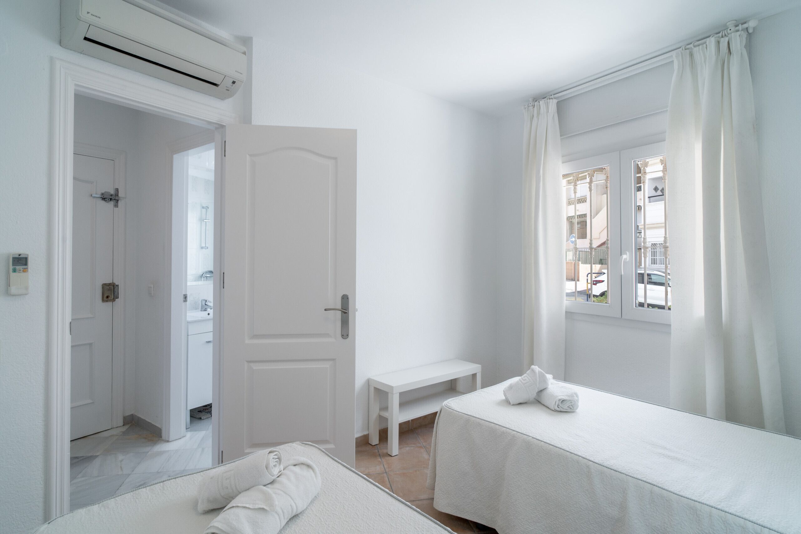 Une chambre d’hôtel avec un lit, un banc et une fenêtre avec des rideaux.
