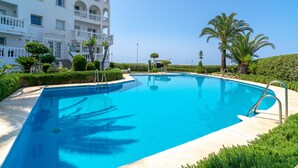 Une piscine entourée d’une végétation luxuriante et entretenue, ainsi qu’un bâtiment blanc doté de balcons.