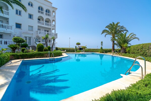 A swimming pool surrounded by manicured greenery and a white building with balconies. - Stella Maris Beachfront B by Casasol (Nerja)