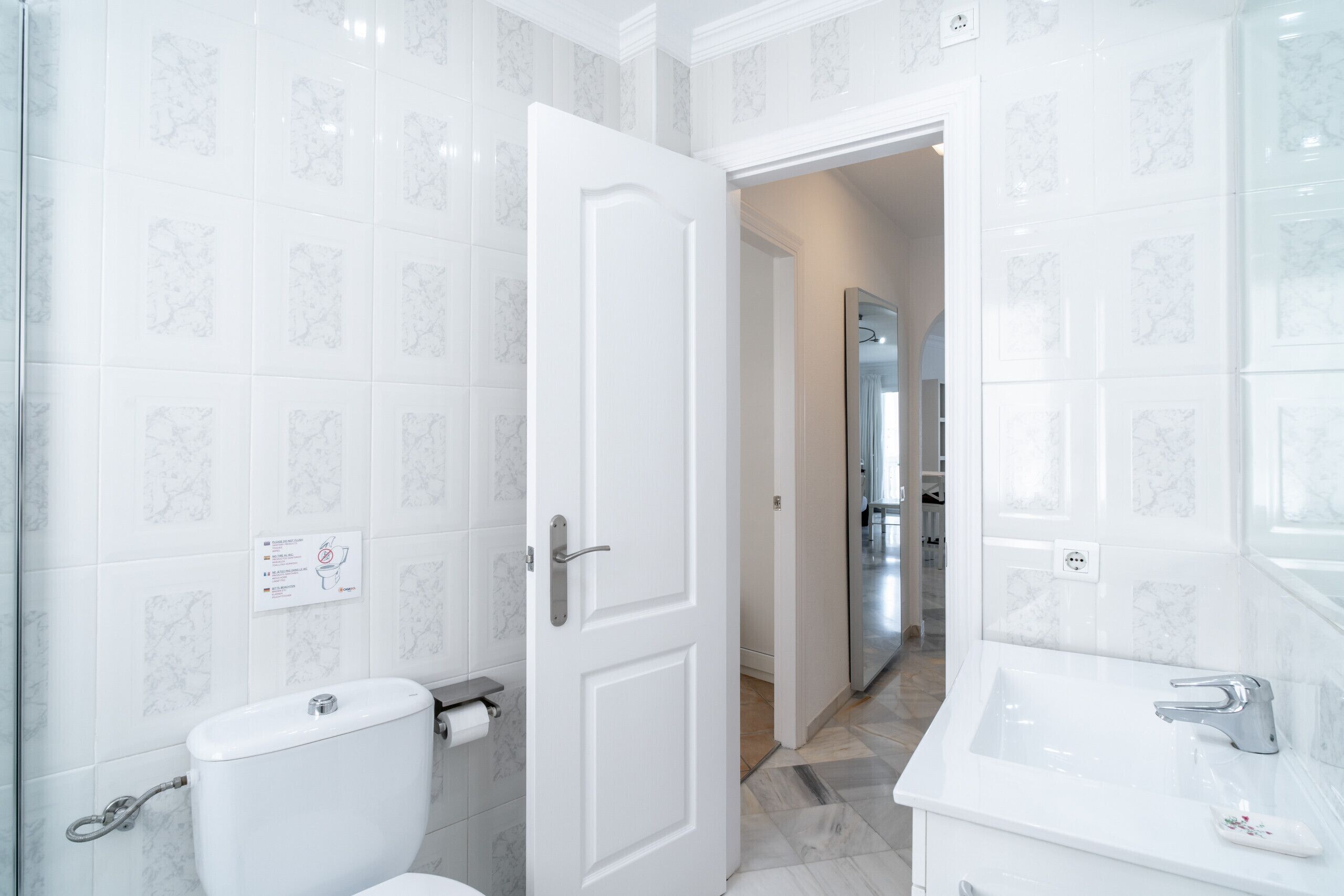Ein Badezimmer mit Toilette, Waschbecken und einer Tür zu einem anderen Raum.