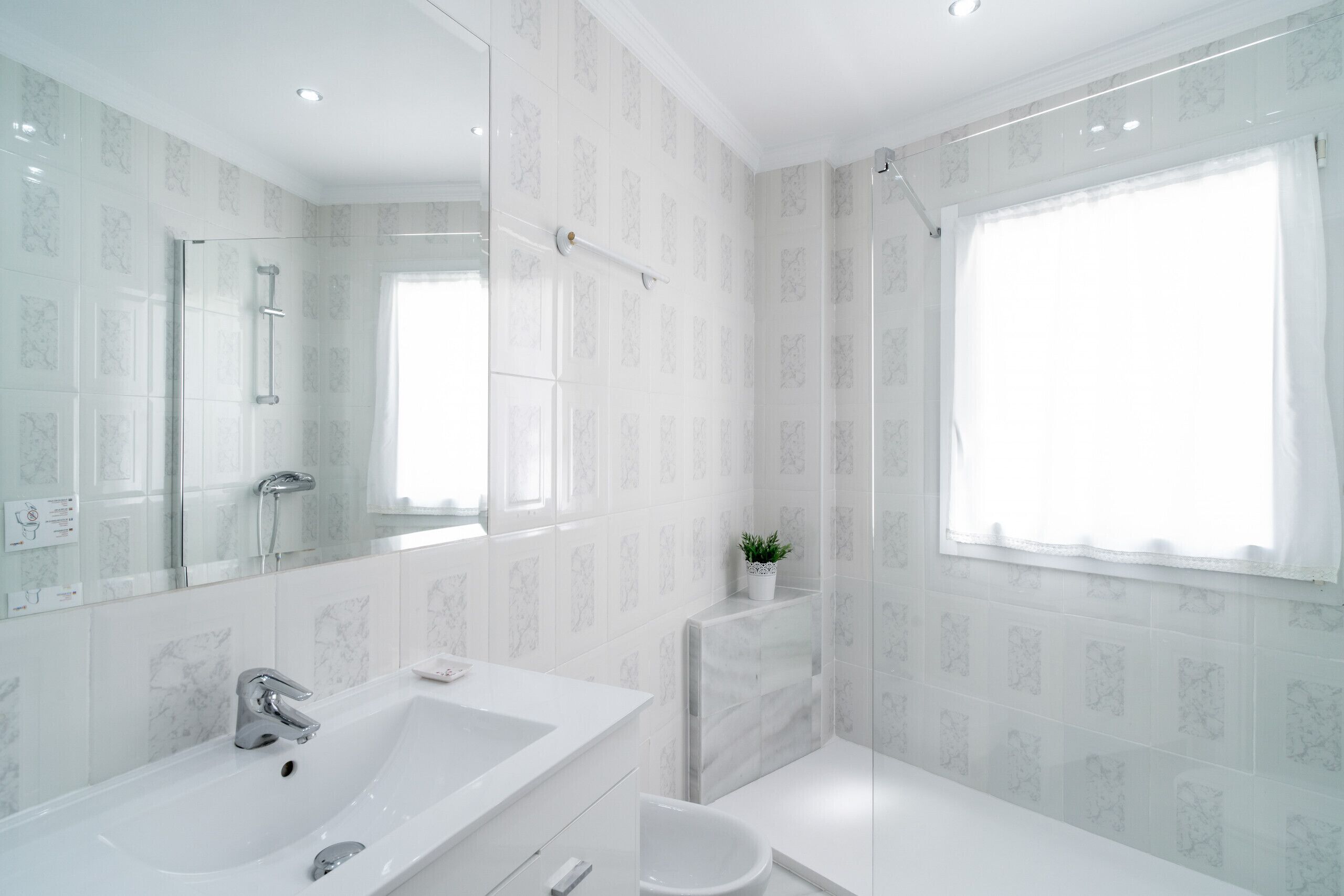 A modern bathroom with a large mirror, a bathtub, a shower, and a toilet.